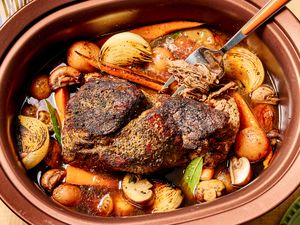 A slowcooked pot roast with vegetables in a crockpot shown with a fork lifting a piece of the roast