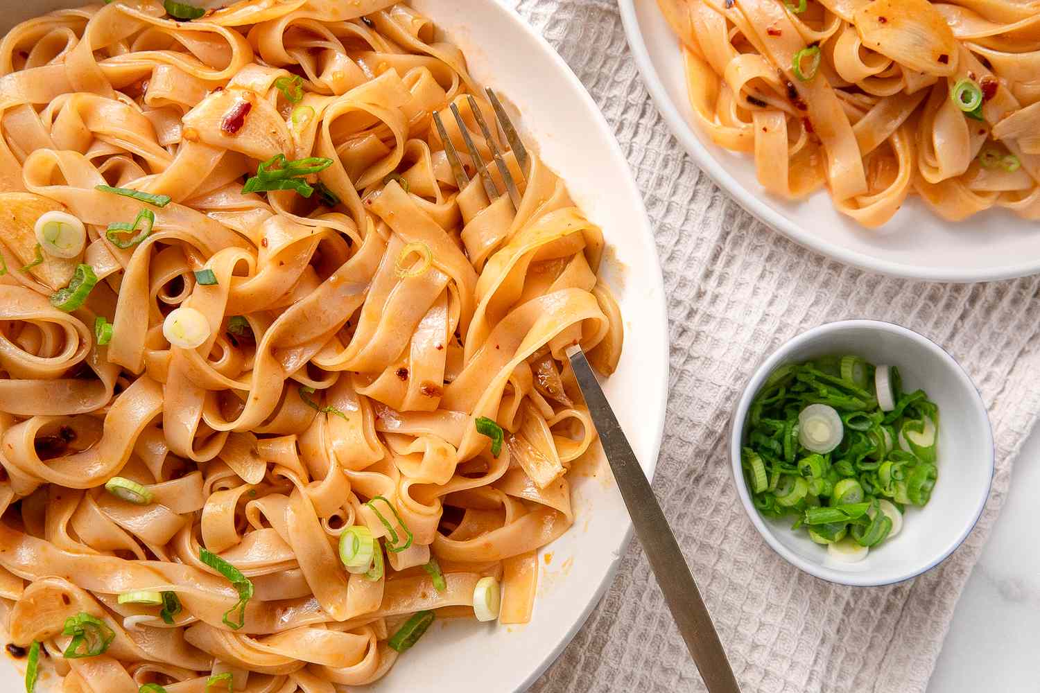 Overhead shot of a serving plate with broad rice noodles in a garlic sauce, garnished with slices scallions