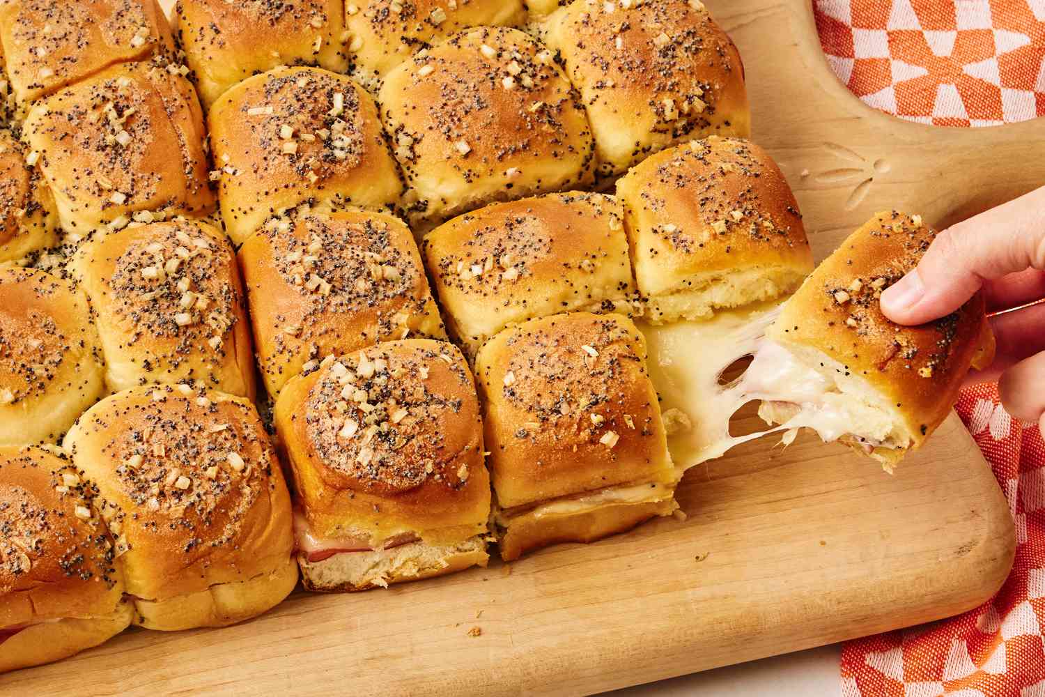 Funeral Sandwiches on a serving board, one sandwich being pulled by a hand, delicious looking cheese stretch