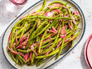 pickled green beans on a platter next to a glass of water and a stack of plates