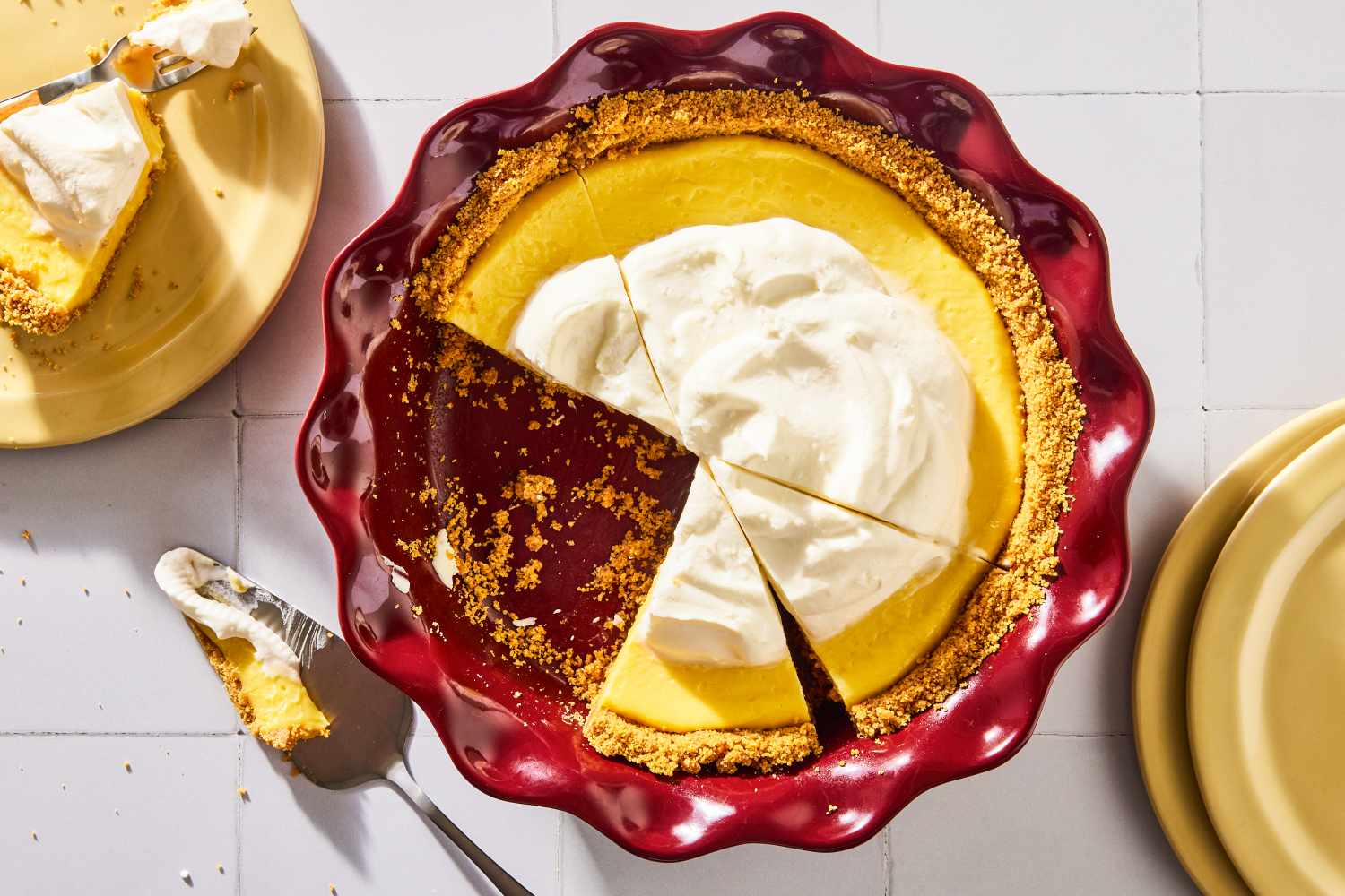 A pie served in a red dish with whipped topping and a slice removed on a table with plates nearby