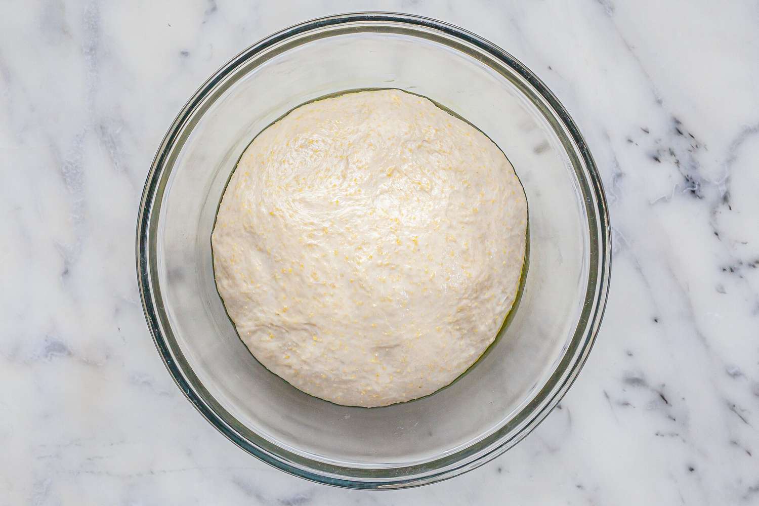 Risen dough for Homemade Chicago-Style Deep Dish Pizza in a glass bowl.