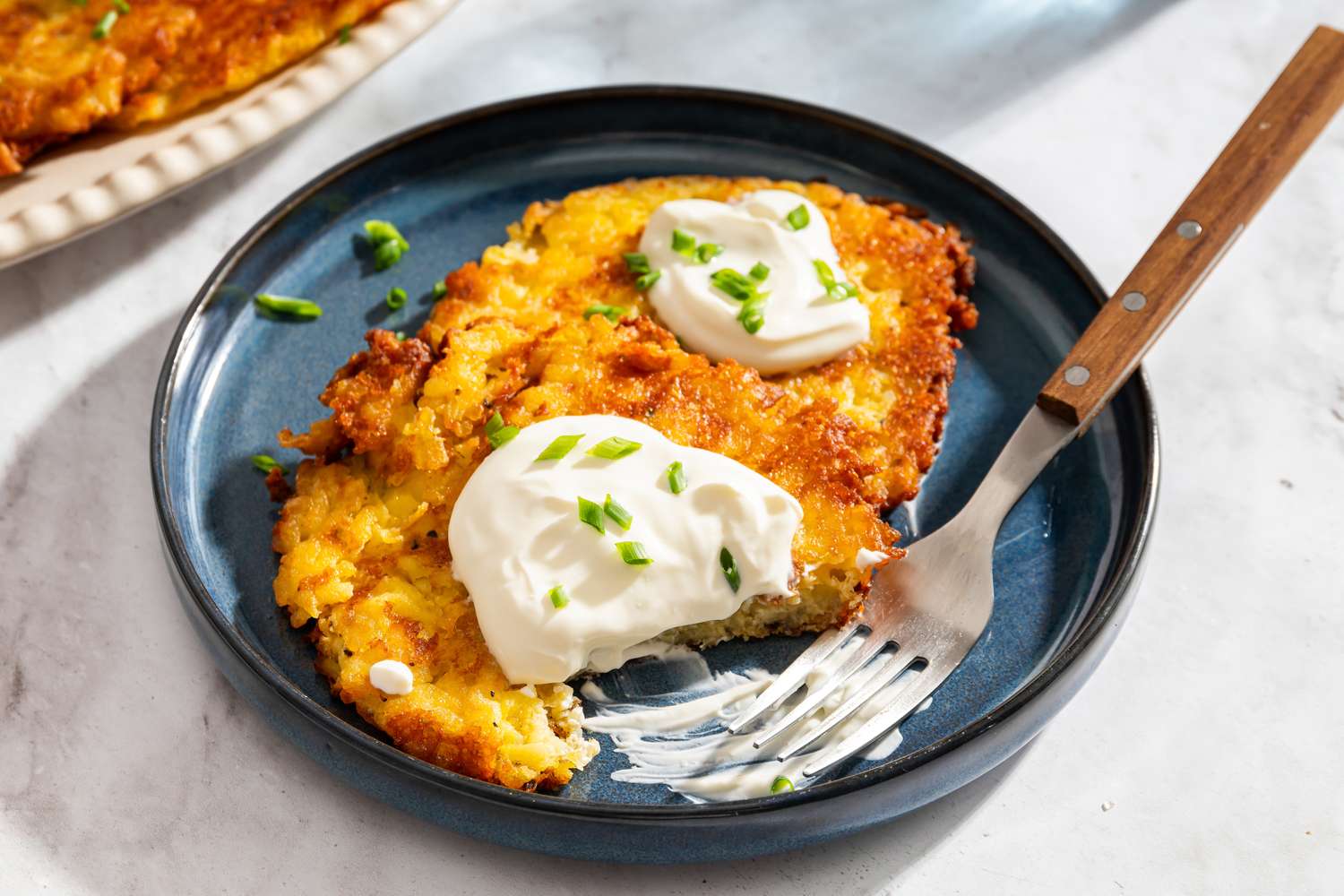 A serving of potato latkes topped with sour cream and chives on a plate with a fork