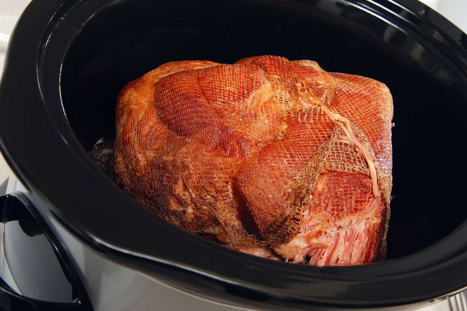Ham being cooked in a crockpot partially netted ready for slow cooking process