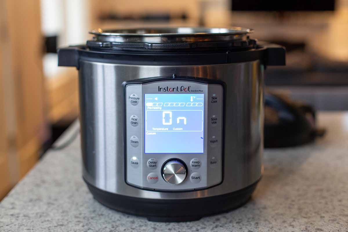 An instant pot is sitting on a kitchen counter and the lid is off. The screen says "On".