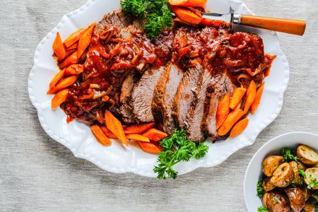 Jewish Brisket on a Plate with Carrots and Parsley and a Bowl of Potatoes
