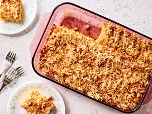 Overhead view of a glass baking dish of pineapple coconut cake with two slices removed next to two small plates with slices along with three forks