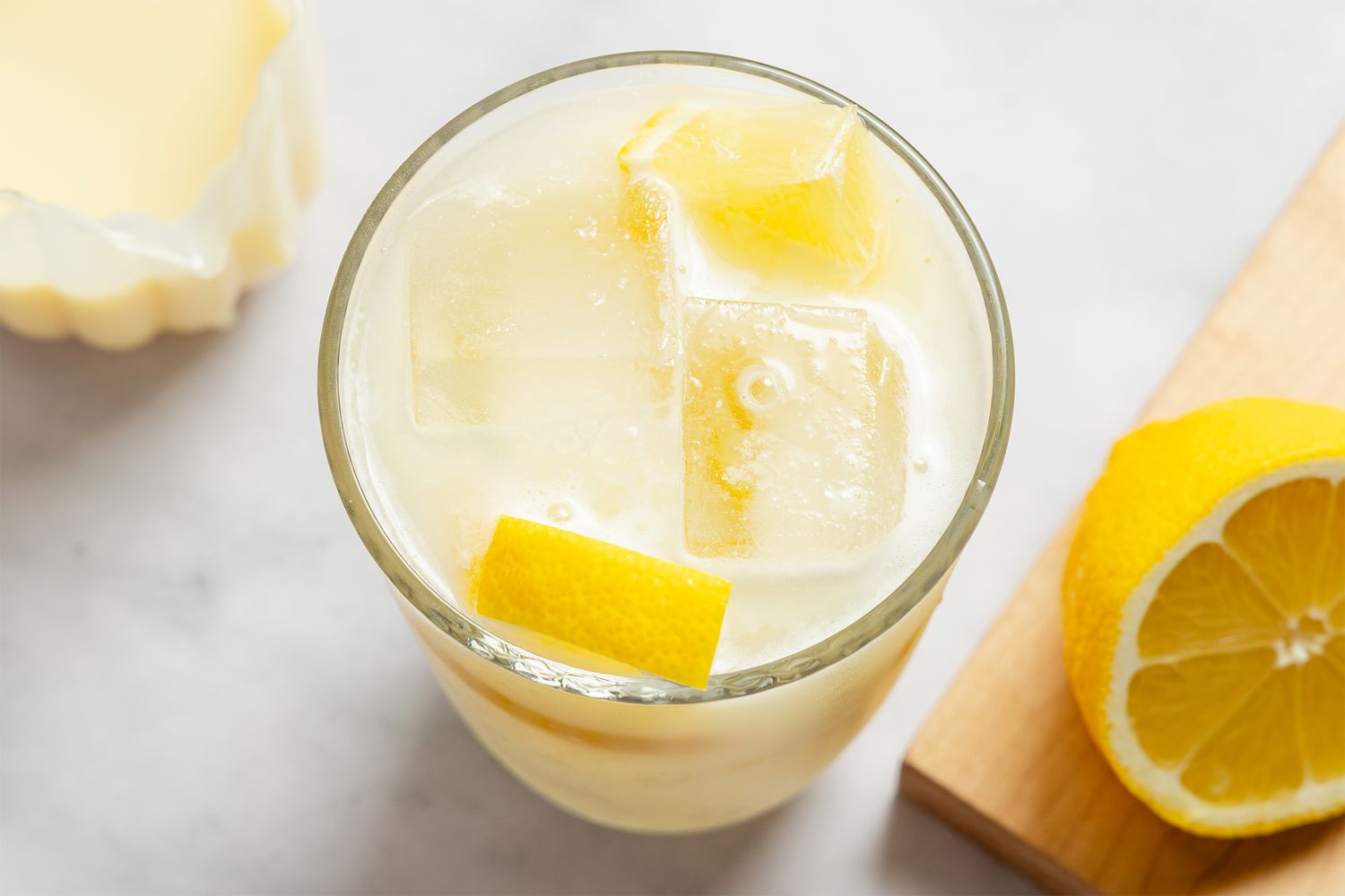 A glass of creamy lemonade next to a halved lemon and lemon zest