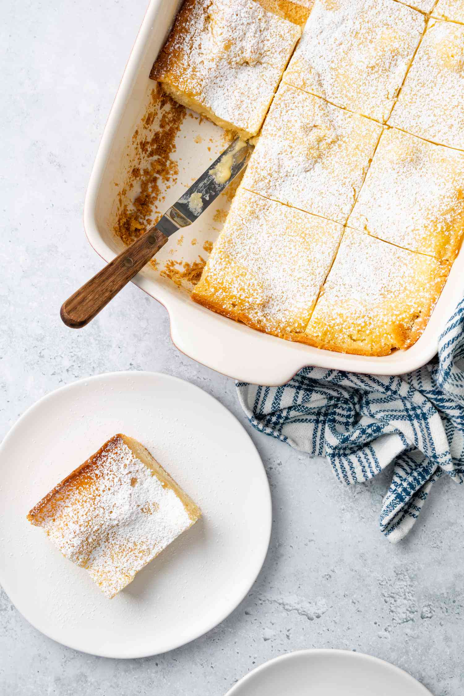 Gooey Butter Cake Cut into Pieces in a Baking Pan with a Piece on a Plate Next to It