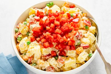 A bowl of potato salad with diced tomato garnish on top containing peas carrots and creamy dressing