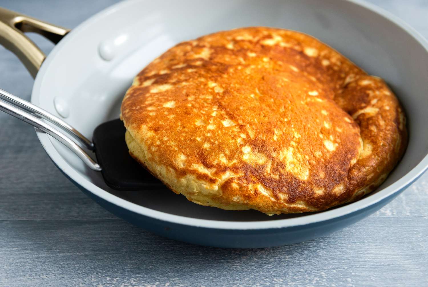 A pancake being flipped with a spatula in a nonstick skillet