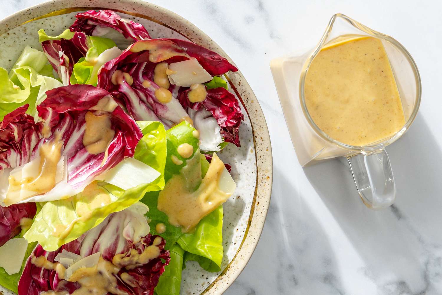 A plate of salad with lettuce and radicchio, served with a container of light vinaigrette dressing on the side