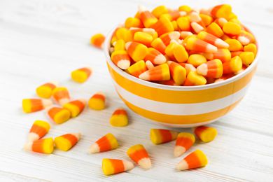A bowl of candy corn with some candy corn scattered on a countertop