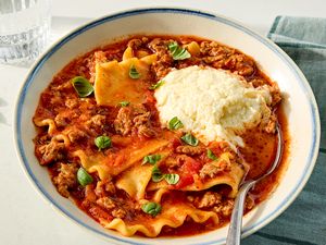 A bowl of lasagna soup topped with ricotta cheese and basil