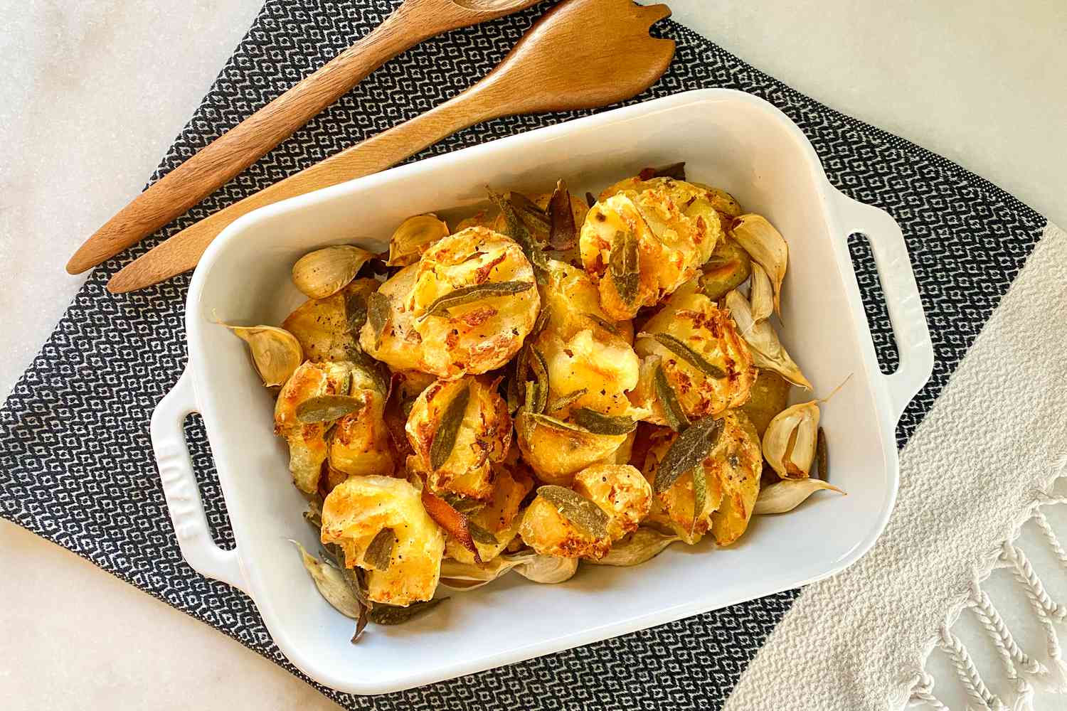 Roasted potatoes in a white serving dish, showing crispy sage leaves and roasted garlic cloves