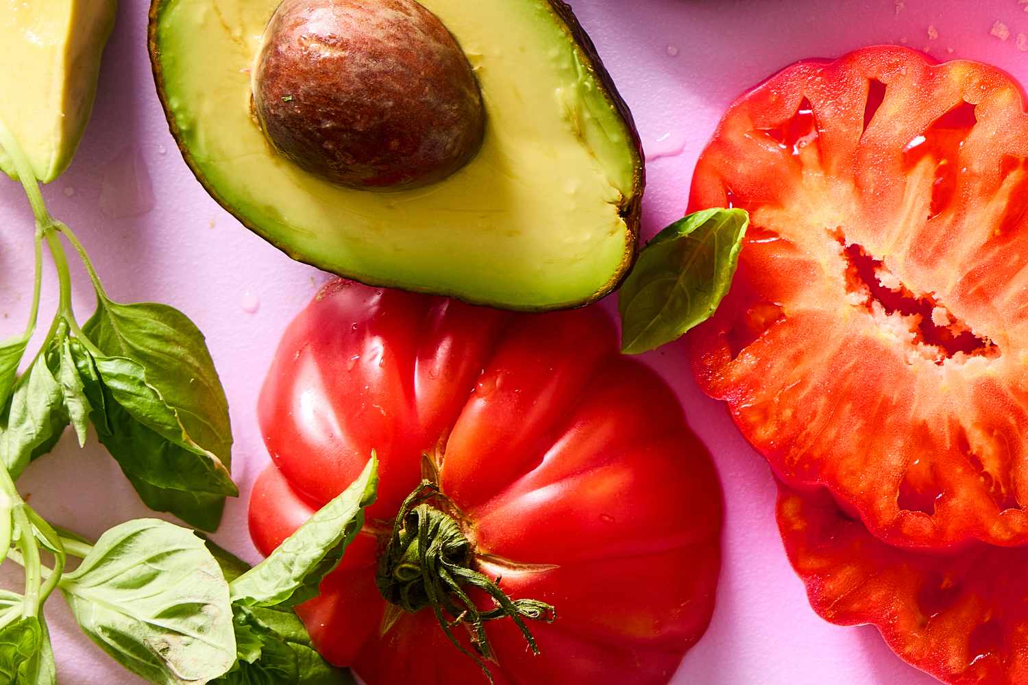 Sliced avocado, tomato halves, and basil leaves arranged on a surface