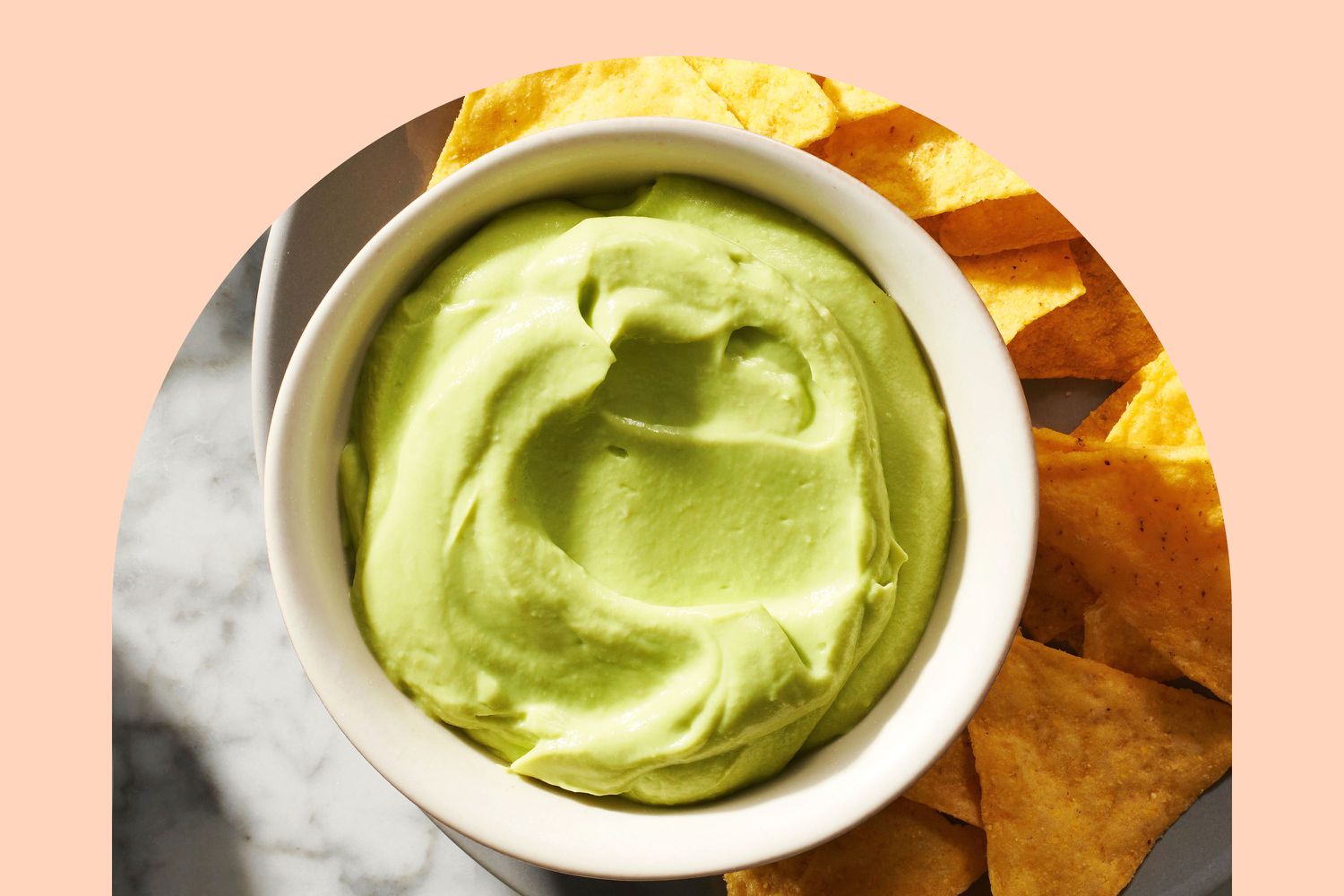Super smooth guacamole in a white ramekin with tortilla chips on the side