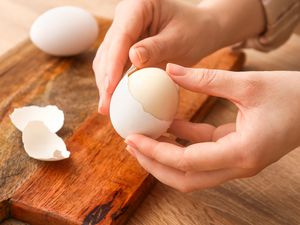 Woman peeling boiled egg at wooden table, closeup