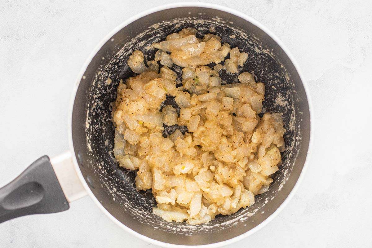 A saucepan with sauteed onions, chicken broth and flour mixed together to start the cheese sauce for potato casserole without canned cream soup.