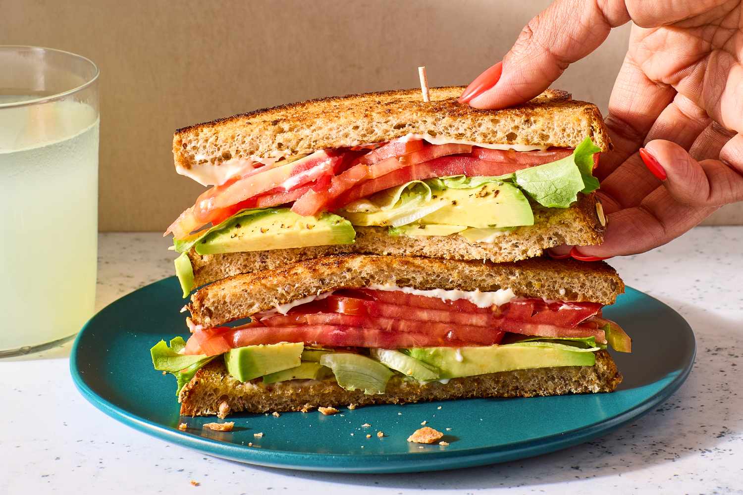A sandwich with sliced tomatoes, avocado, butter lettuce, and mayonnaise on toasted whole-wheat bread