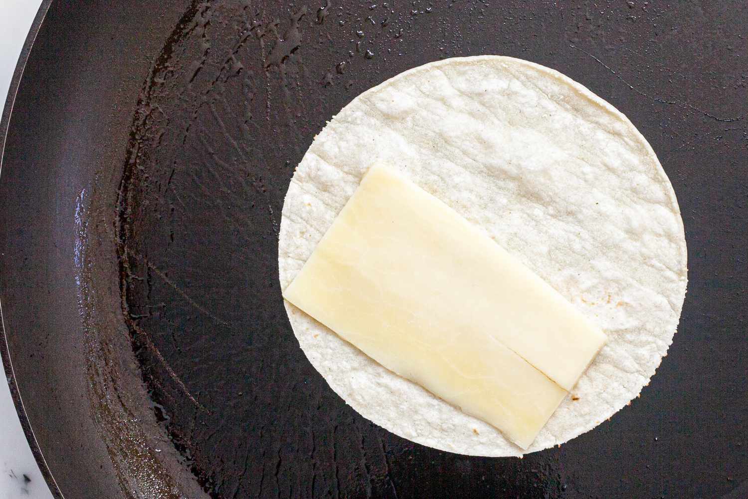 Small tortilla in a skillet with cheese on half of it to make a vegetarian tacos recipe.