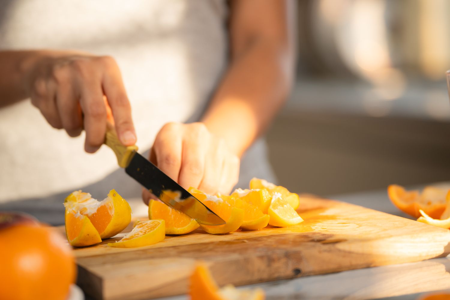 Side view of a person cutting up oranges with a knife on a wooden cutting board