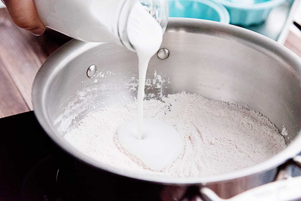 Dry ingredients for this pantry dessert are in a large stock pot. Coconut milk is being poured into the pot.
