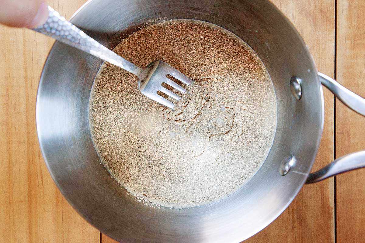 A fork is stirring dry yeast and milk in a saucepan.