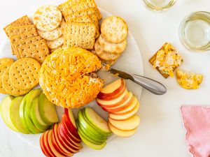 Overhead view of a white plate of a ham ball appetizer surrounded by various crackers and apple slices
