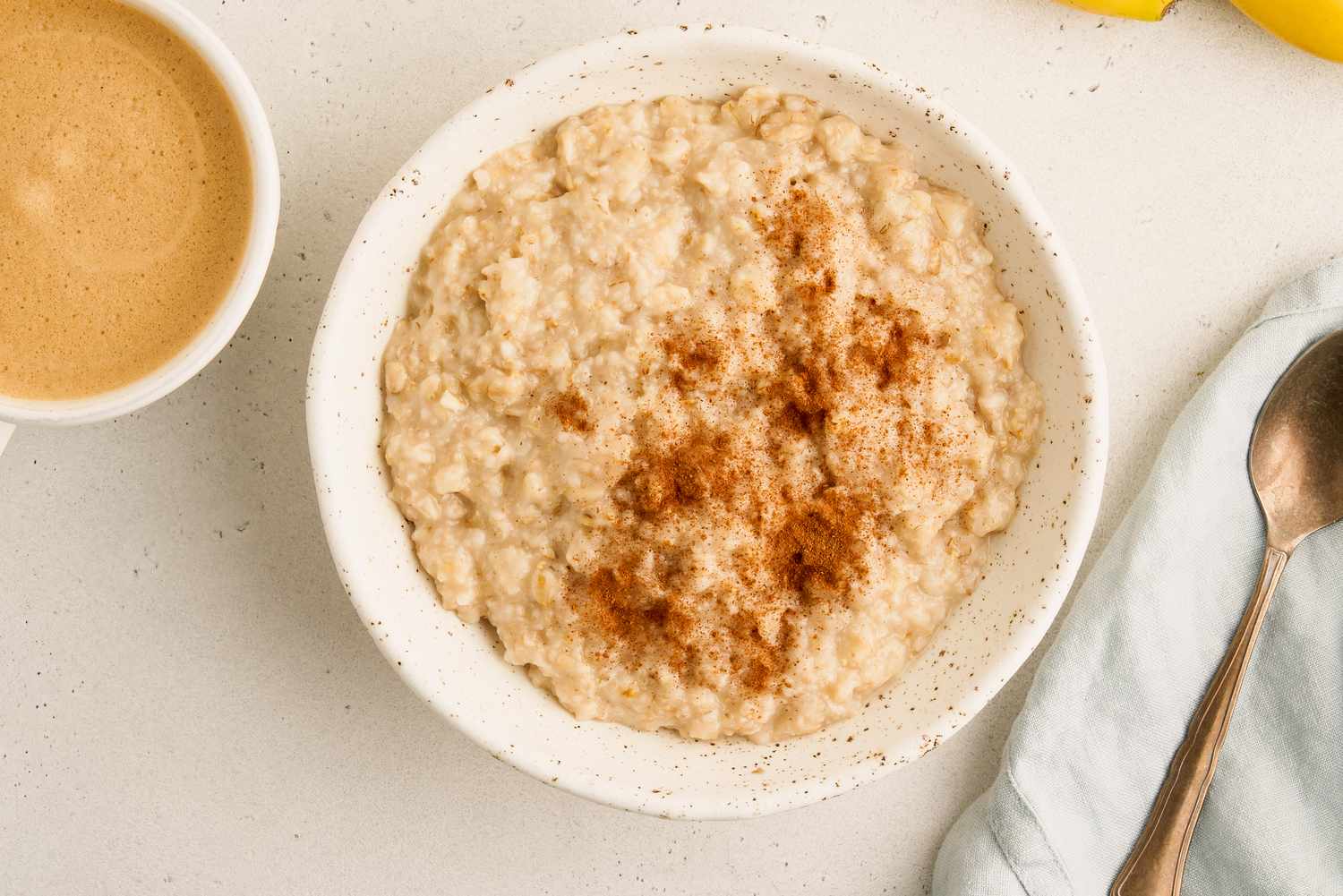 Bowl of oatmeal topped with cinnamon served with coffee and a spoon nearby
