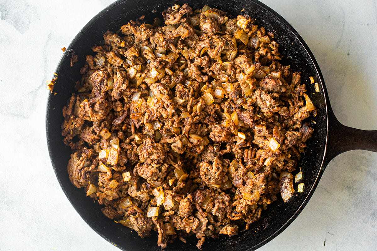 Ground beef in a cast iron skillet for Easy Slow Cooker Beef and Bean Chili.