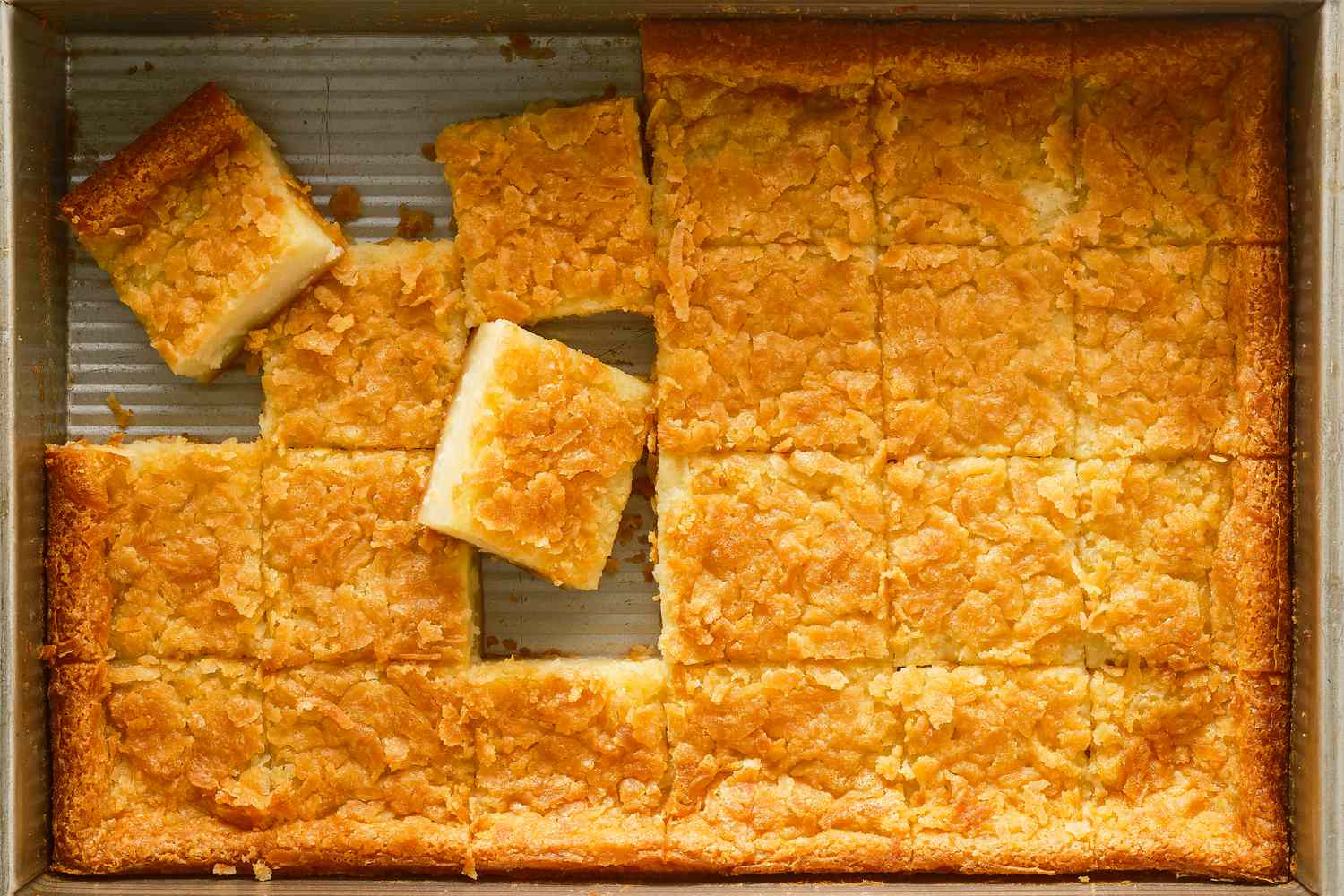 Overhead shot of butter mochi baked in a rectangular baking dish, cut into squares with some pieces taken out