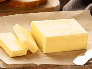 A stick of butter with slices arranged on parchment accompanied by a butter knife