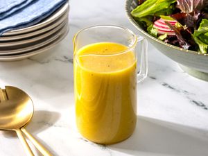 Ginger dressing in a small container at a table setting with a stack of plates, a bowl of salad, and salad utensils