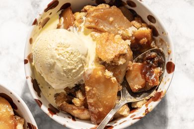 Closeup view of a serving of caramel apple cobbler topped with a scoop of vanilla ice cream in a bowl