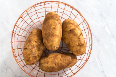 Four raw potatoes in a wire basket on a marble kitchen counter