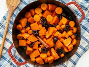 overhead view of Carrot and Sweet Potato Tzimmes in a roasting pan with a wooden spoon