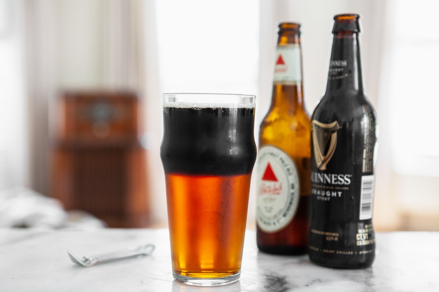 Glass of Black and Tan Next to Two Bottles of Beer and a Bottle Opener 