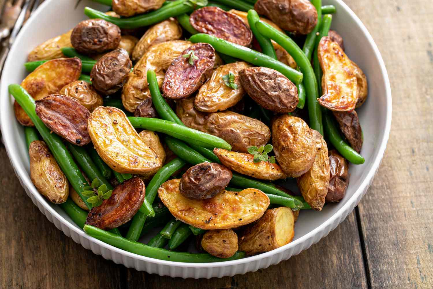 Roasted crispy fingerling potatoes with green beans in a serving bowl with herbs and spices, spring side dish