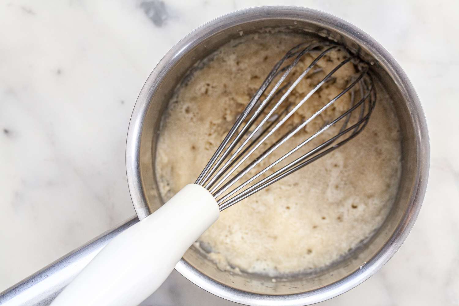 Adding milk to the roux to make white sauce or béchamel sauce.