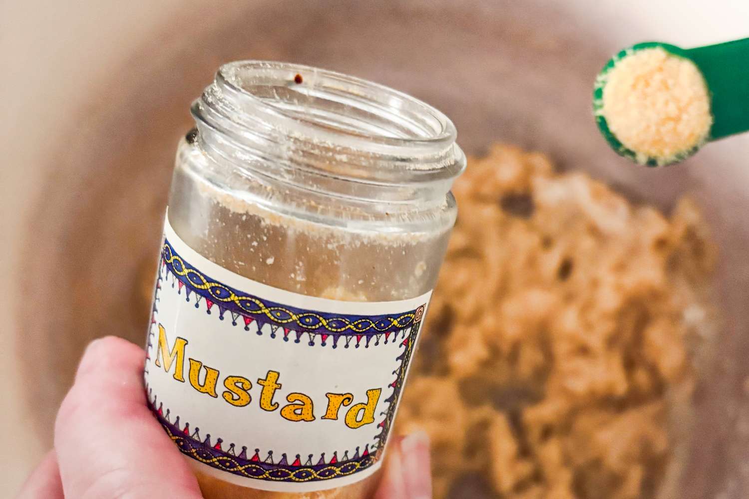 A person adding powdered mustard from a jar into a mixture in a bowl