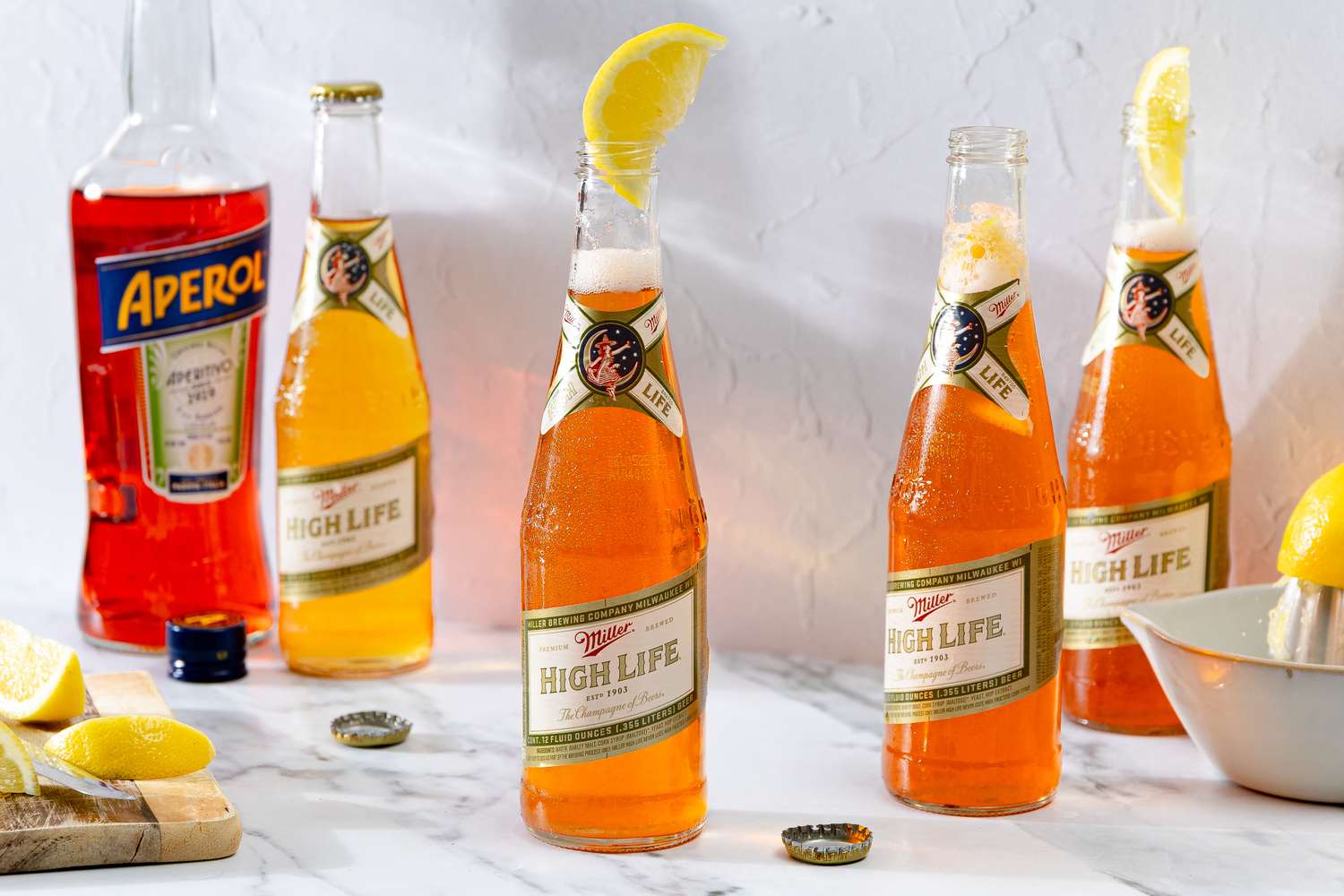 Bottles of Miller High Life beer mixed with Aperol rimmed with lemon wedges