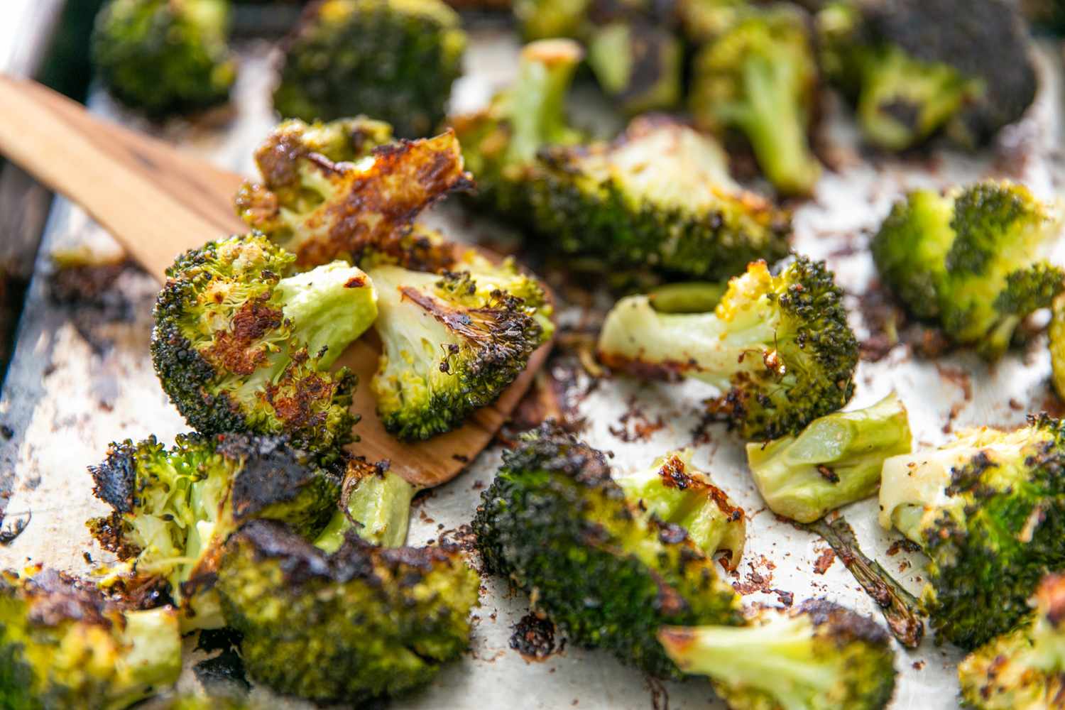 Roasted broccoli pieces on a baking sheet with a wooden spatula
