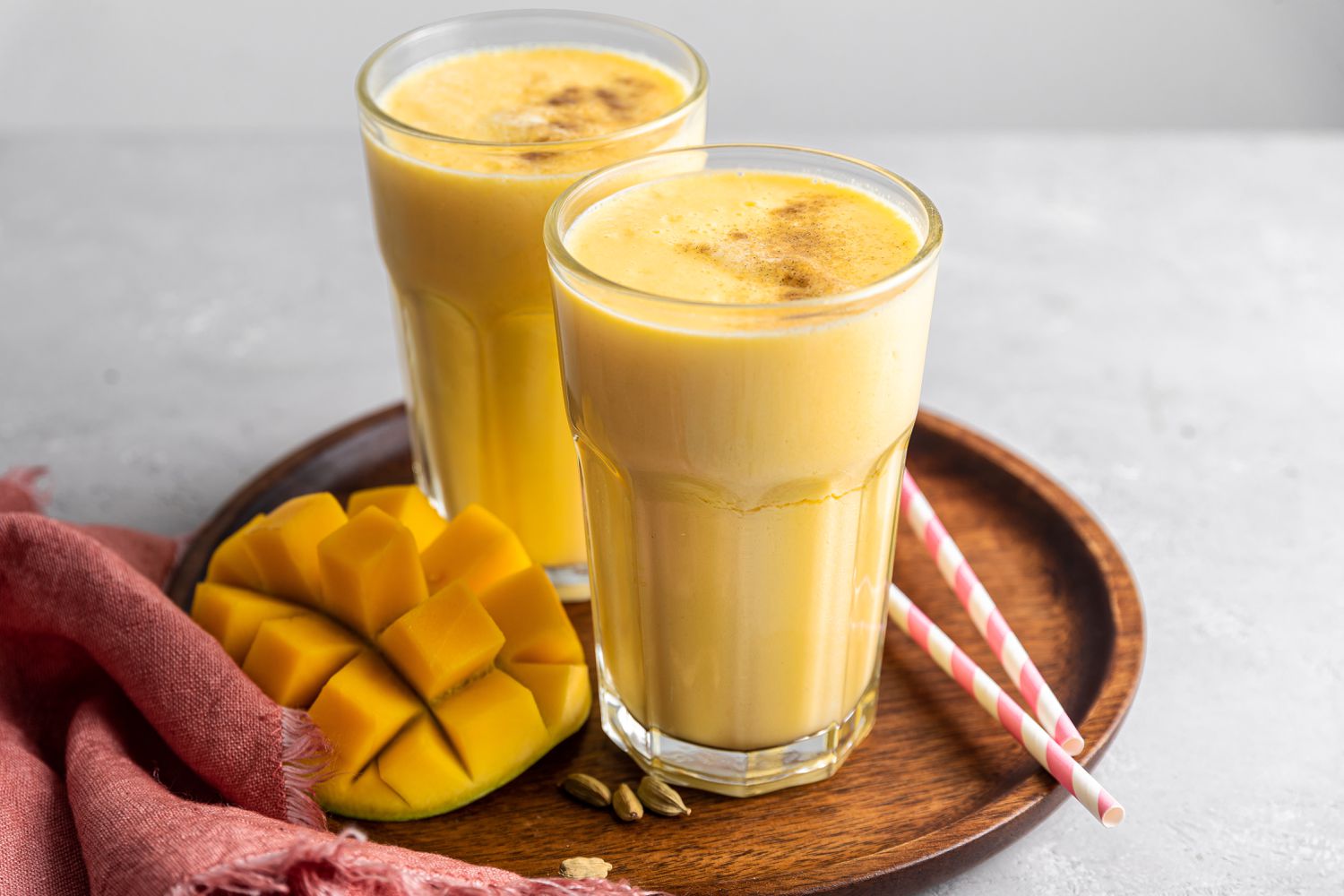 Two Glasses of Mango Lassi on Tray with Cubed Mango and Straws