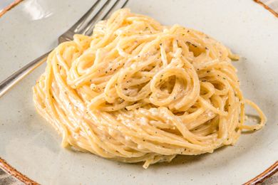 A plate of spaghetti with cream sauce and black pepper fork on the side