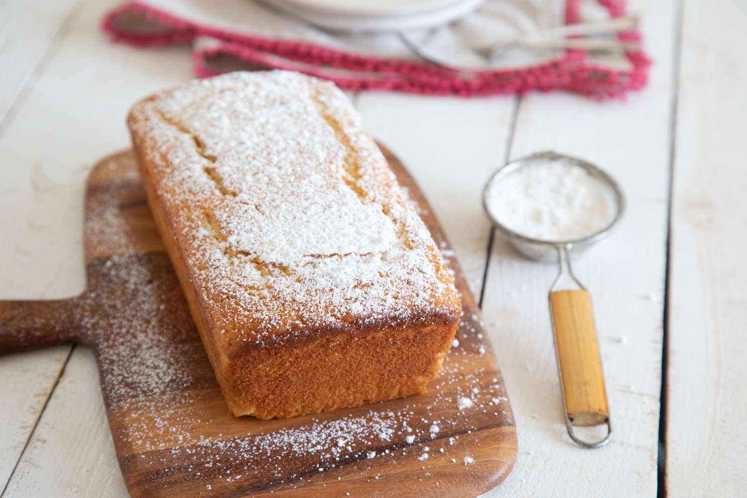 Easy Yogurt Cake dusted in powdered sugar and set on a wooden paddle.