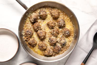French Onion Meatballs in a Pan Next to Two Bowls and a Spoon on Table Cloth
