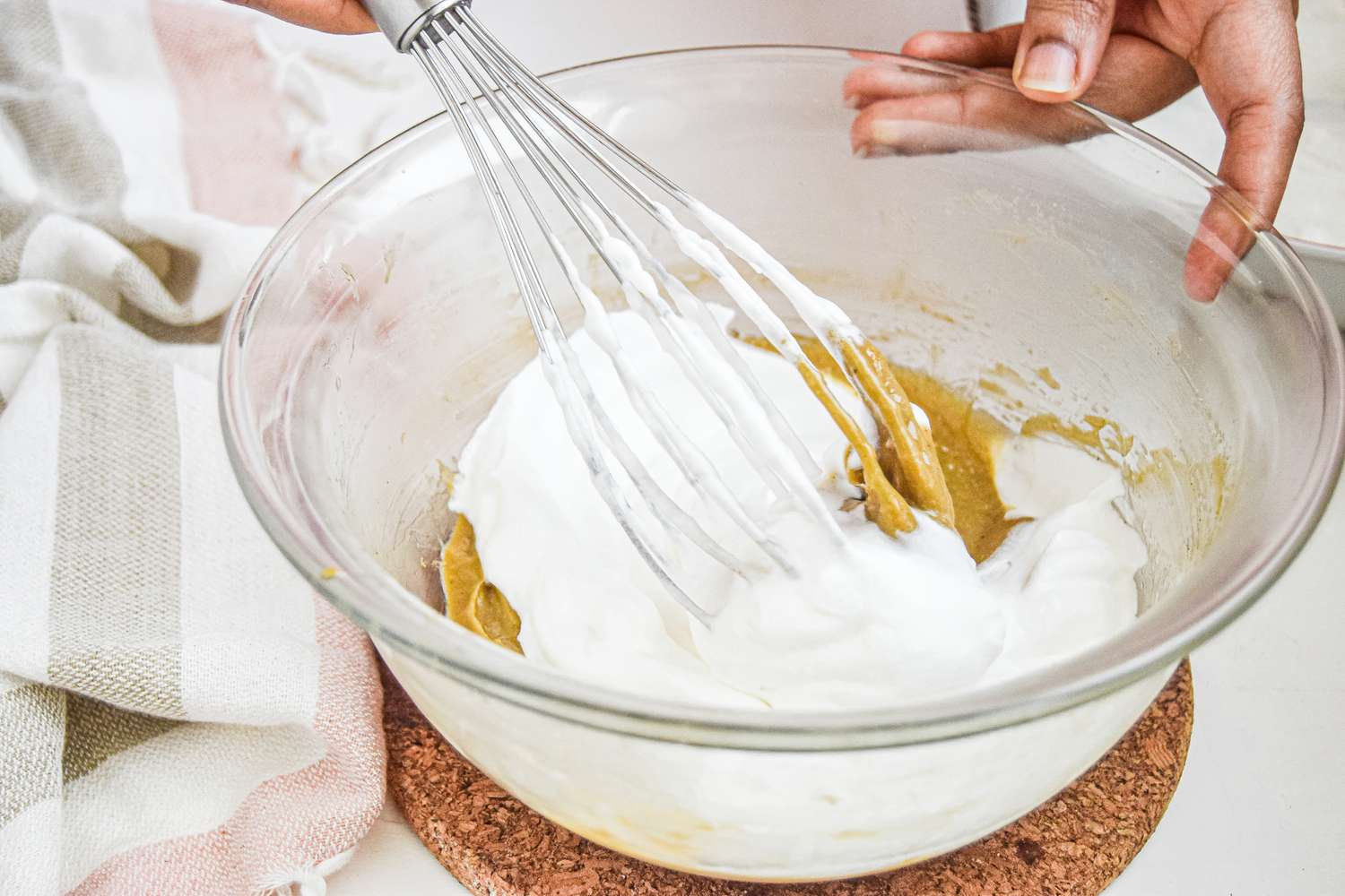 Whisking custard into whipped cream in a large glass bowl to make a custard dessert.