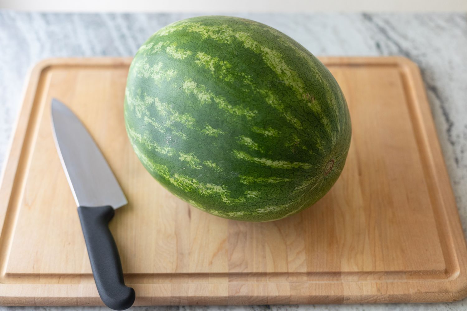 A whole uncut watermelon on a cutting board with a knife next to it