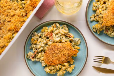 Overhead view of chicken and pasta casserole serving on a blue plate next to a dish of casserole, table napkin and drinking glass with ice and beverage